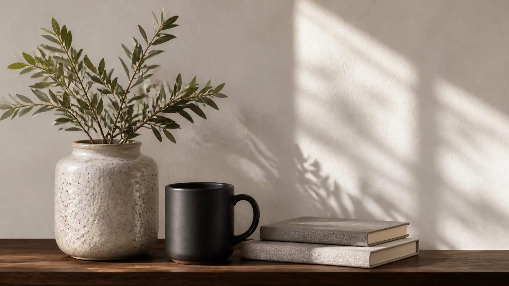 A quiet practice workspace with a ceramic vase, branches, books, and a dark mug